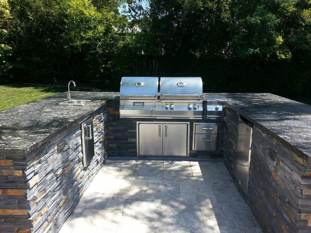Luxury outdoor kitchen in the Hamptons with built-in grill, stone countertops, and custom masonry designTHE HAMPTONS, SECURITY SERVICES, LIGHTING SERVICES, LANDSCAPE SERVICES. EASTHAMPTON, SOUTHAMPTON, WESTHAMPTON, SAG HARBOR planting seasonal coastal