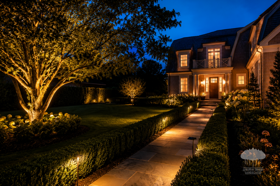 Landscape lighting illuminating a walkway for guest-ready Hamptons landscaping at dusk