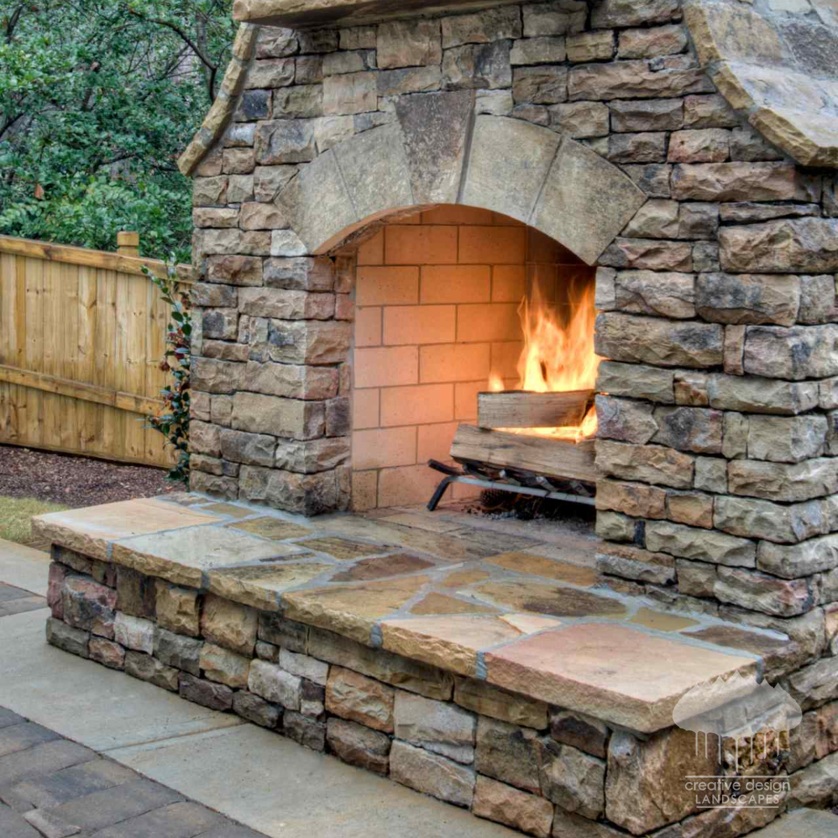 Natural stone outdoor fireplace with an arched firebox and a lit fire