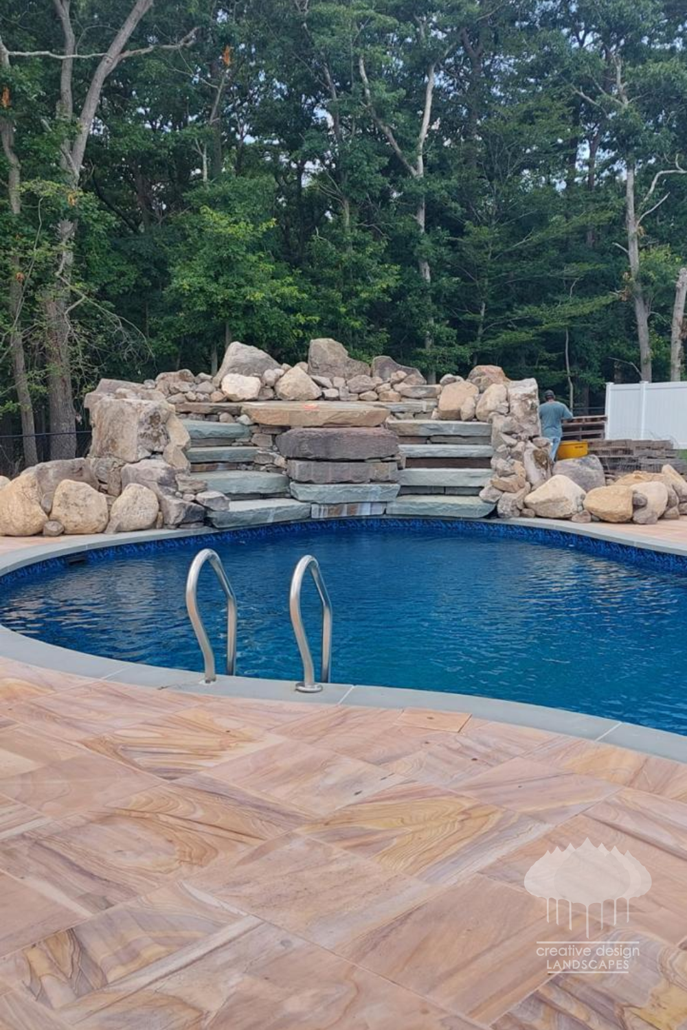 Natural boulder waterfall and stone steps beside a pool with a warm stone deck